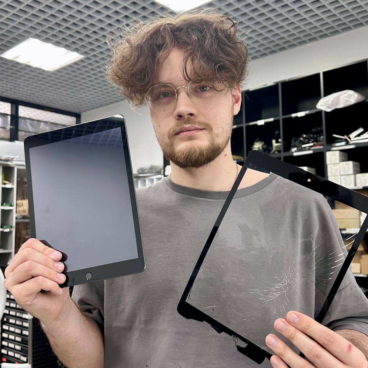 Мастер держит починенный iPad и снятое с него разбитое стекло